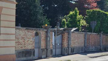 A street view with a brick wall, a metal gate, and a building with a tiled roof.