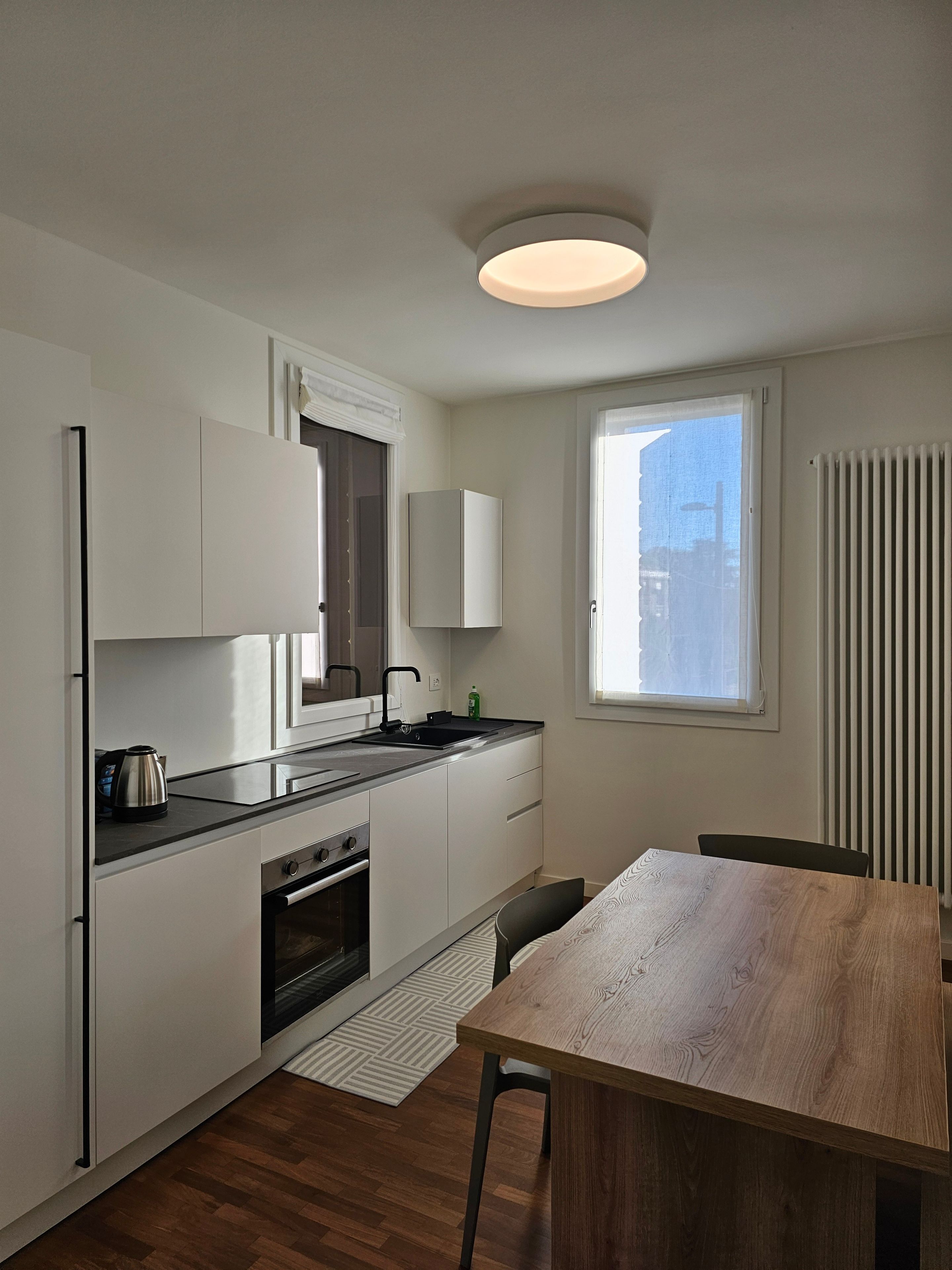 A modern kitchen with white cabinetry, a black countertop, and a wooden dining table.