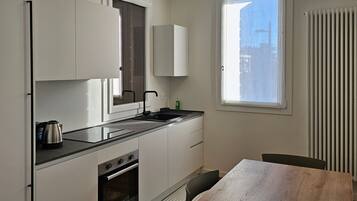 A modern kitchen with white cabinetry, a black countertop, and a wooden dining table.