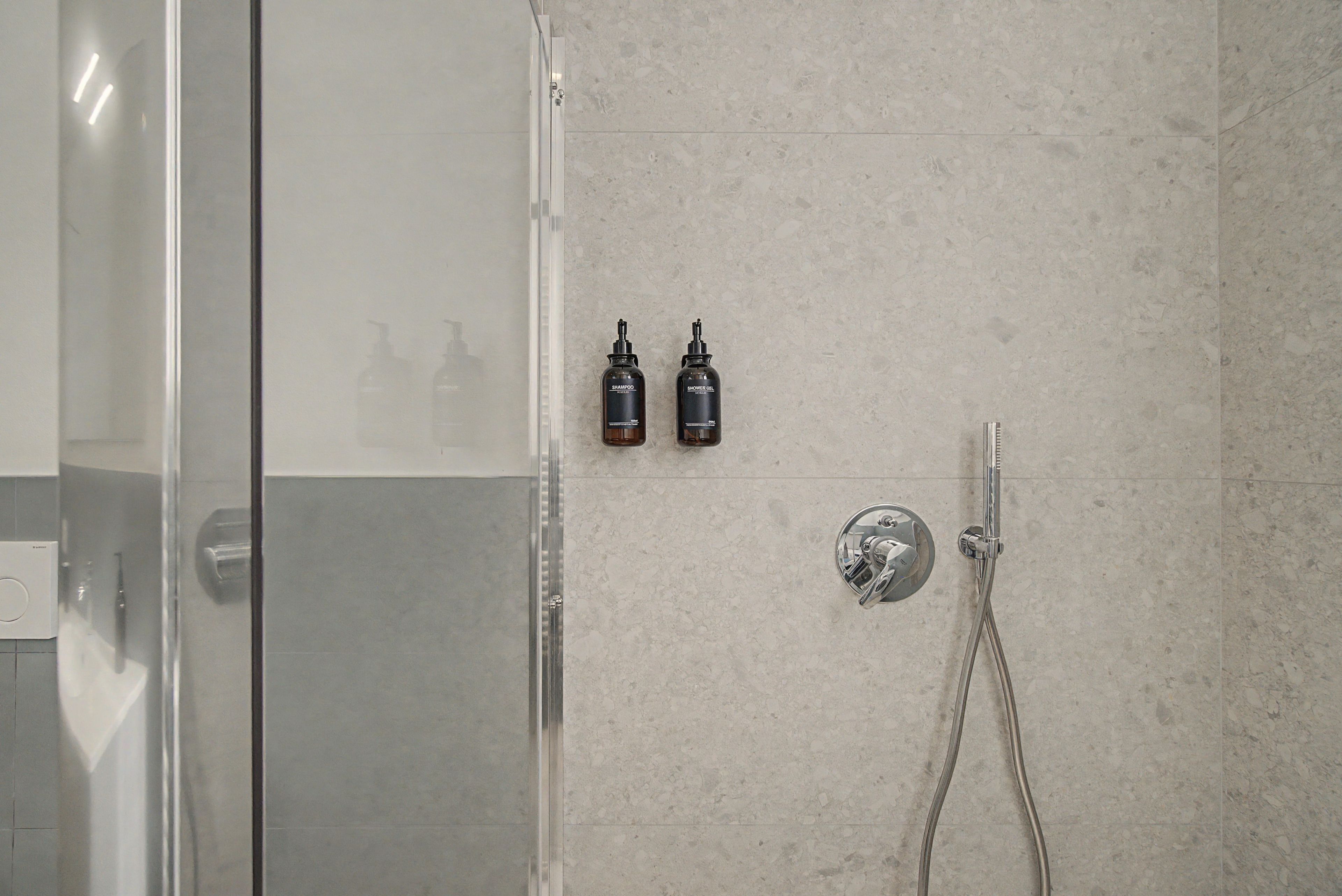 Ein Duschbereich mit Glastür, Handbrause und zwei Flaschen Shampoo sowie Duschgel an der Wand.