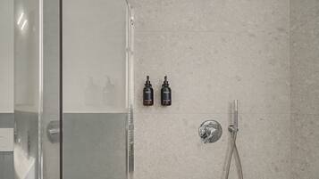 Ein Duschbereich mit Glastür, Handbrause und zwei Flaschen Shampoo sowie Duschgel an der Wand.