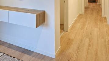 A hallway with a wooden floor, a white wall, and a framed artwork above a wooden bench.