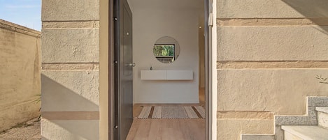 A doorway leading to a room with a wooden floor, a small rug, and a wall-mounted mirror.