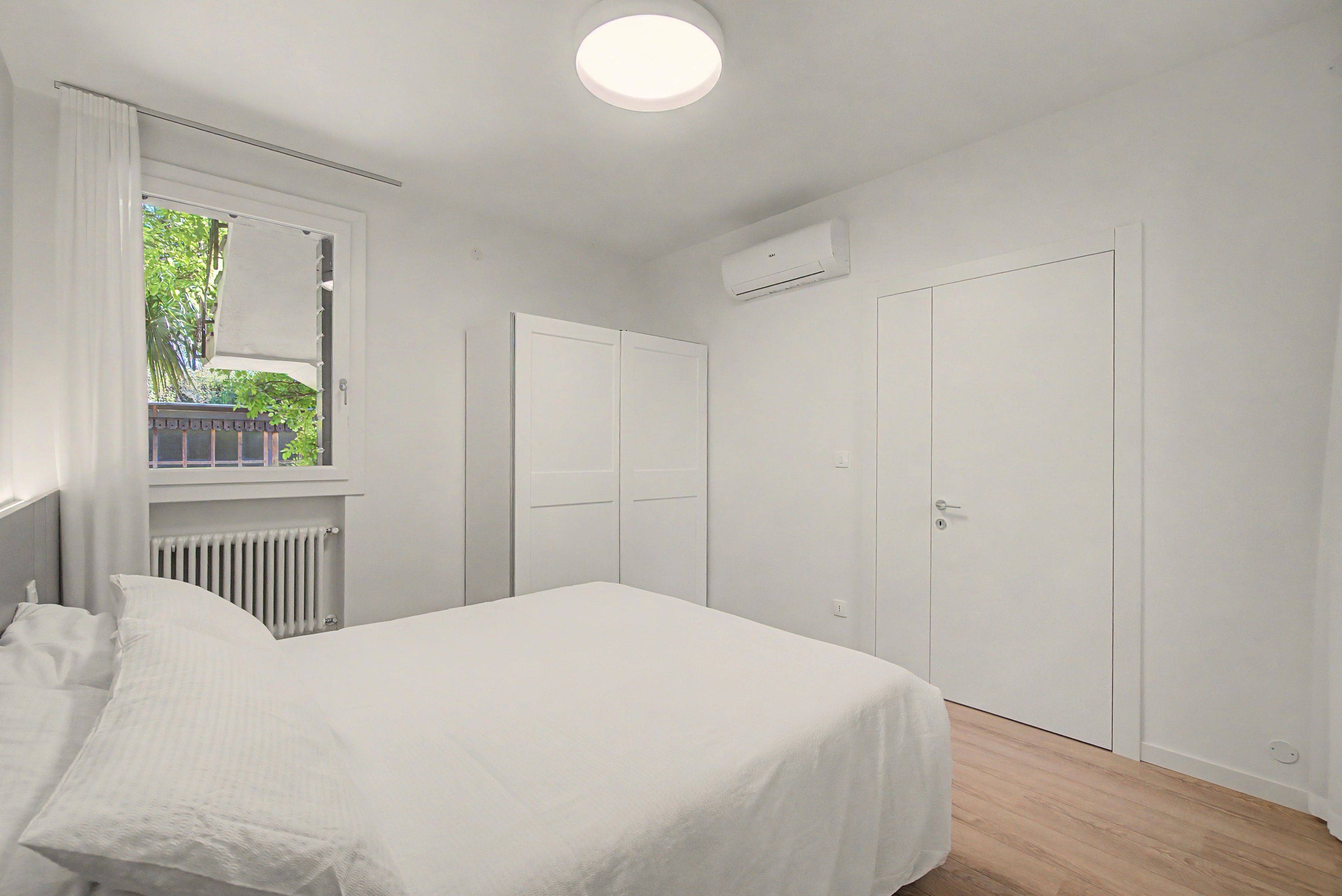 A bedroom with a bed, a window, a radiator, and a door.