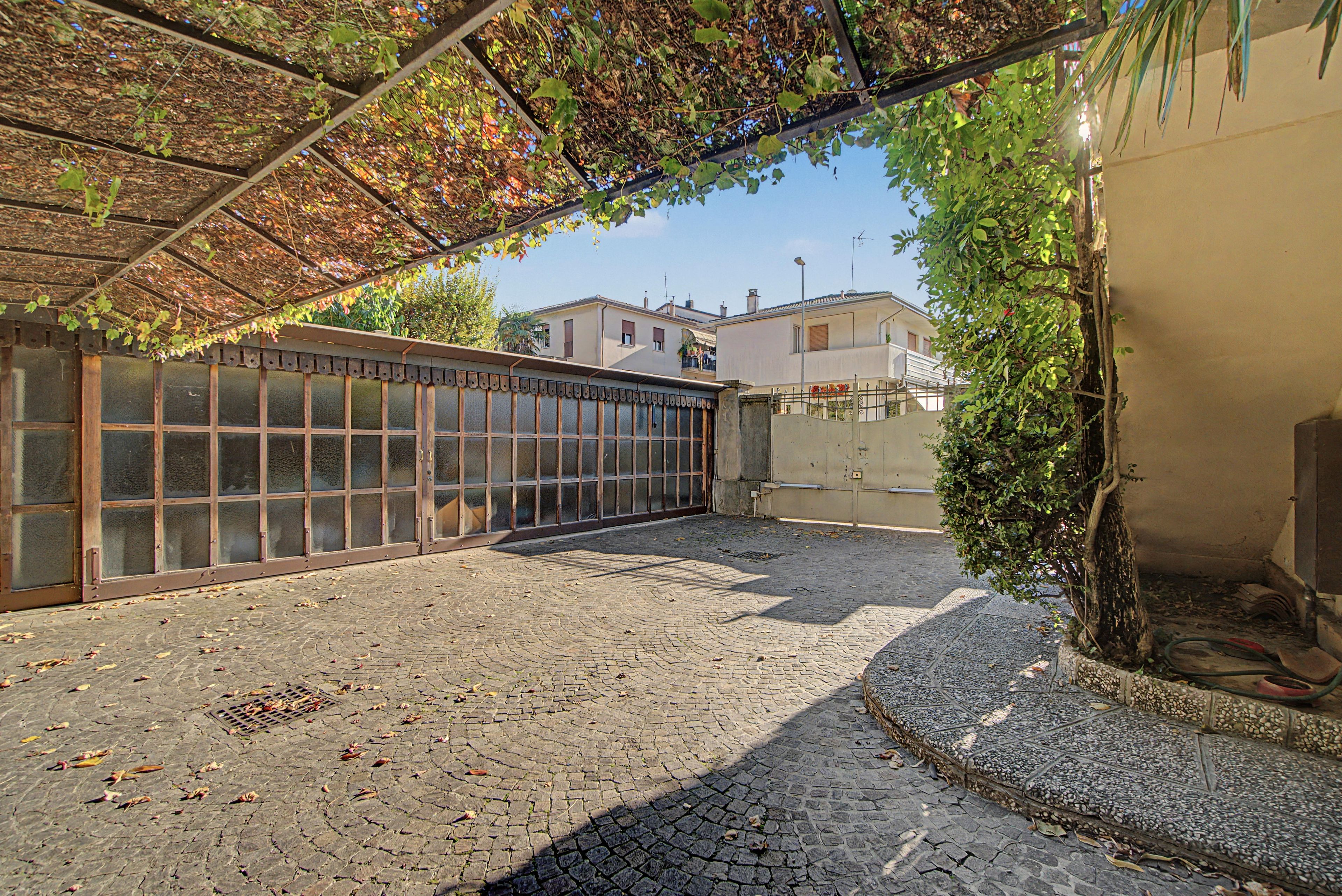 A courtyard with a metal fence, cobblestone ground, and a building in the background.