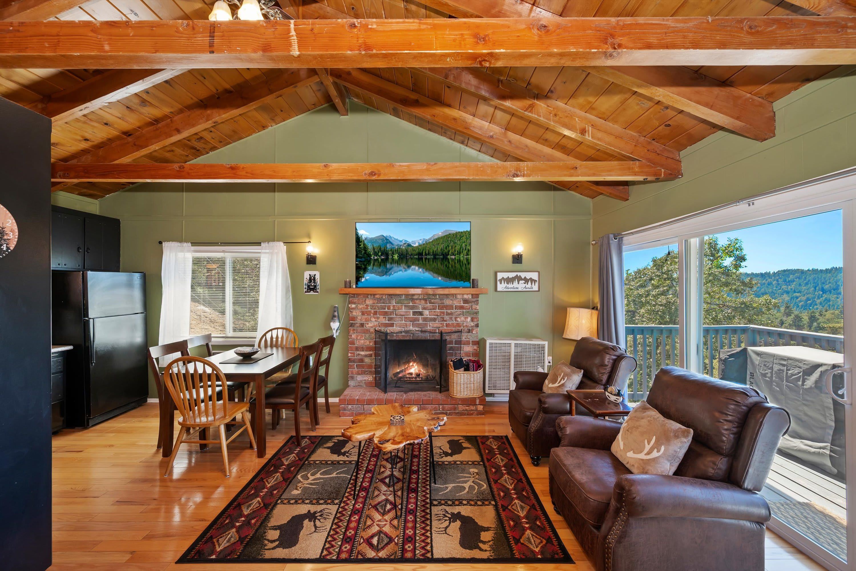 A cozy living room with a fireplace, a dining area, and a view of a lake through large windows.