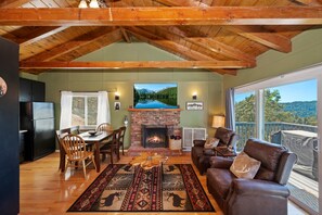 A cozy living room with a fireplace, a dining area, and a view of a lake through large windows.