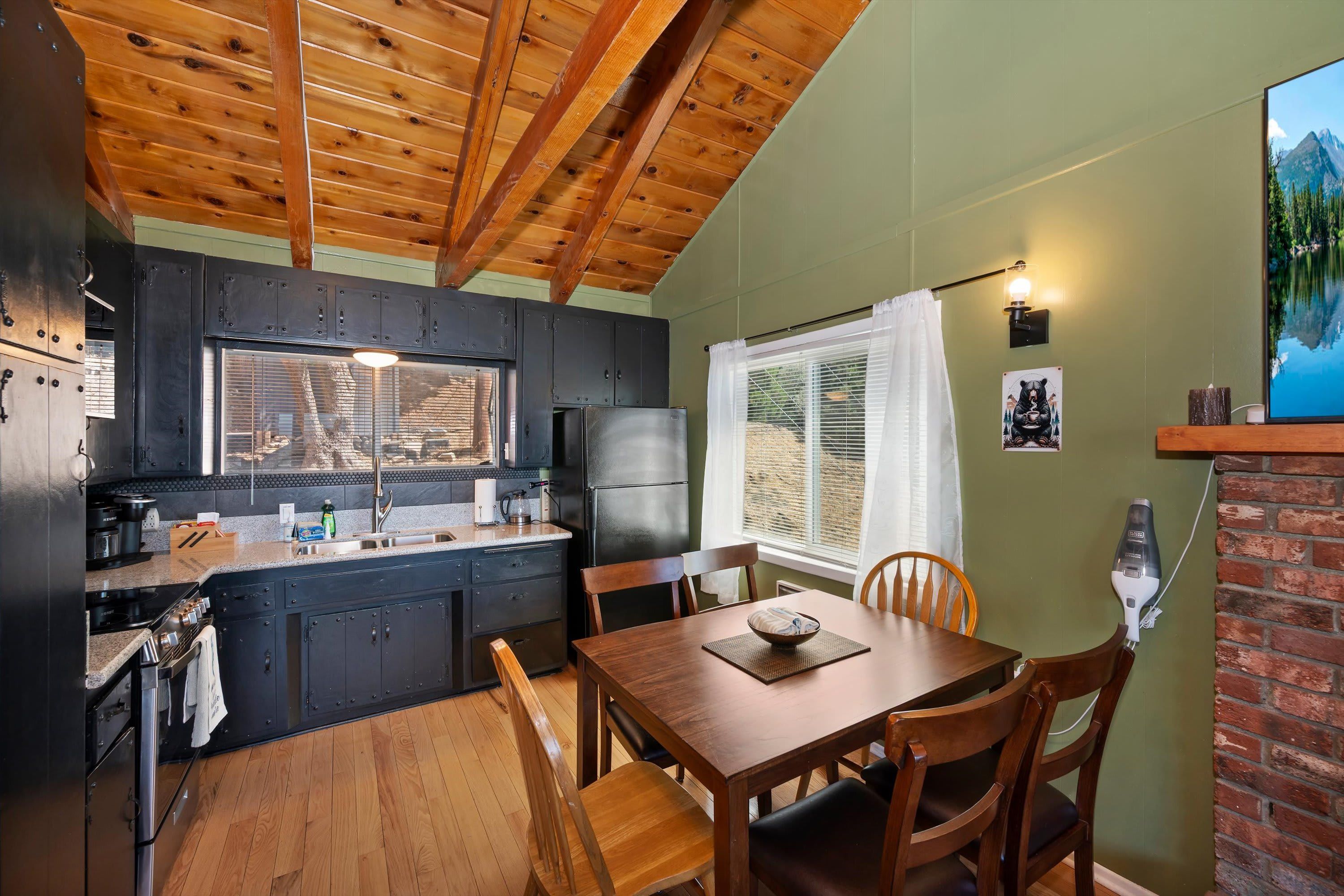 Una cocina compacta con vigas de madera en el techo, un comedor con mesa y sillas, y un ventanal con vistas a la montaña.