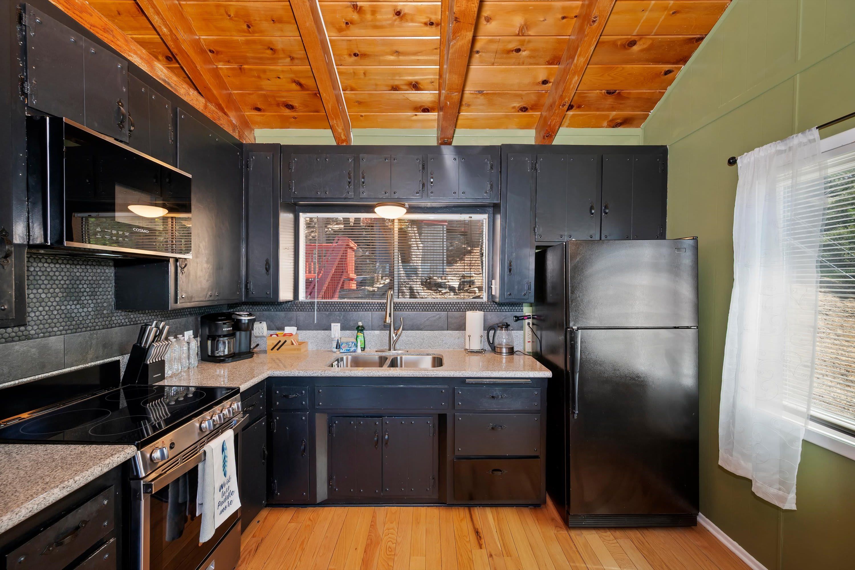 A kitchen with dark cabinets, a stainless steel refrigerator, a stove, and a window with blinds.