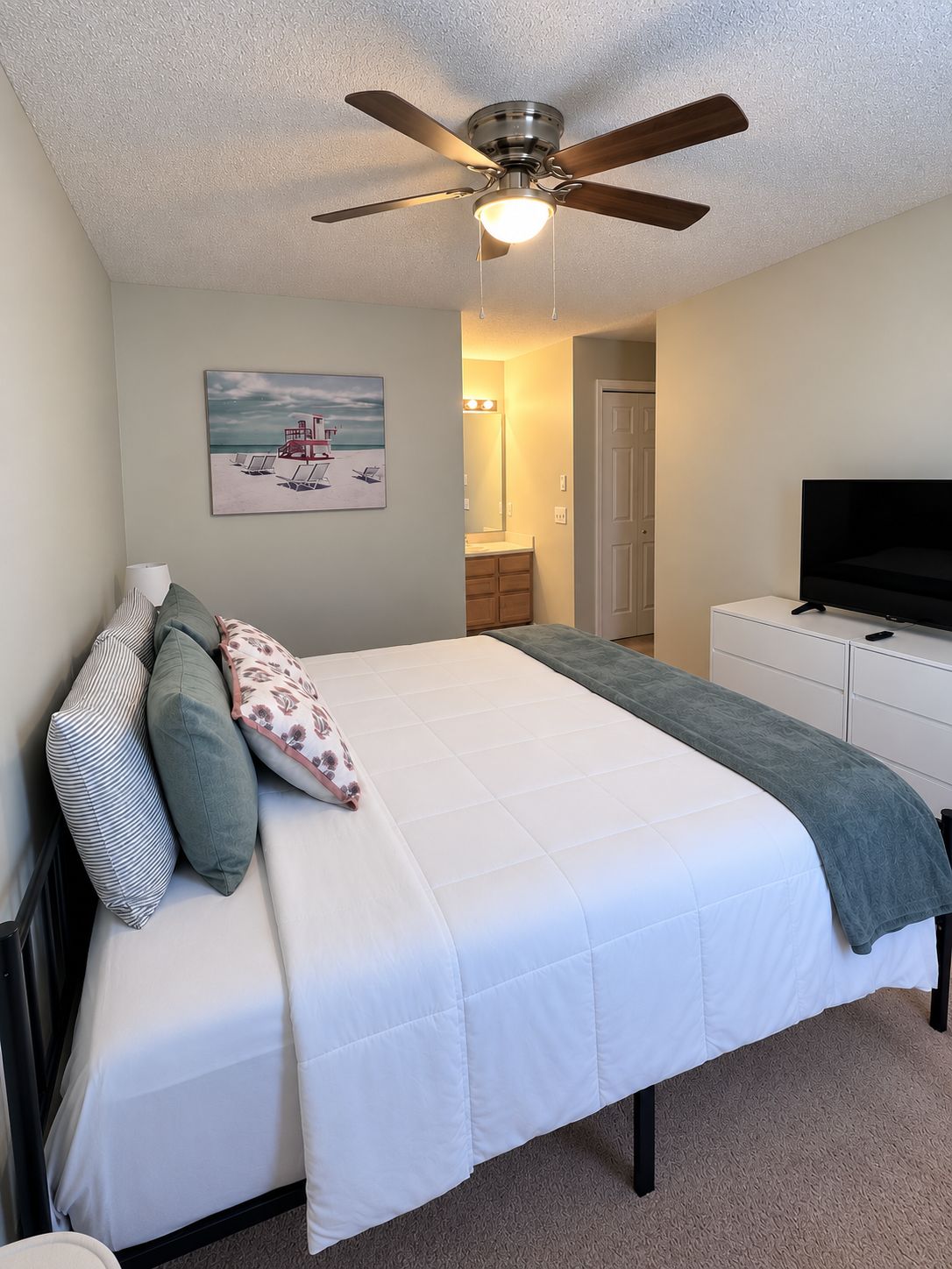 A bedroom with a bed, a ceiling fan, a television, and a painting on the wall.