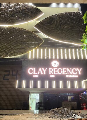 Entrada de un hotel con un letrero iluminado grande que dice 'CLAY REGENCY Hotel Suite Celebrations'.