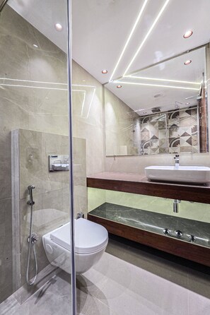 A modern bathroom with a glass-enclosed shower, a white toilet, and a vanity with a mirror. - Clay Regency Hotel   (New Delhi)
