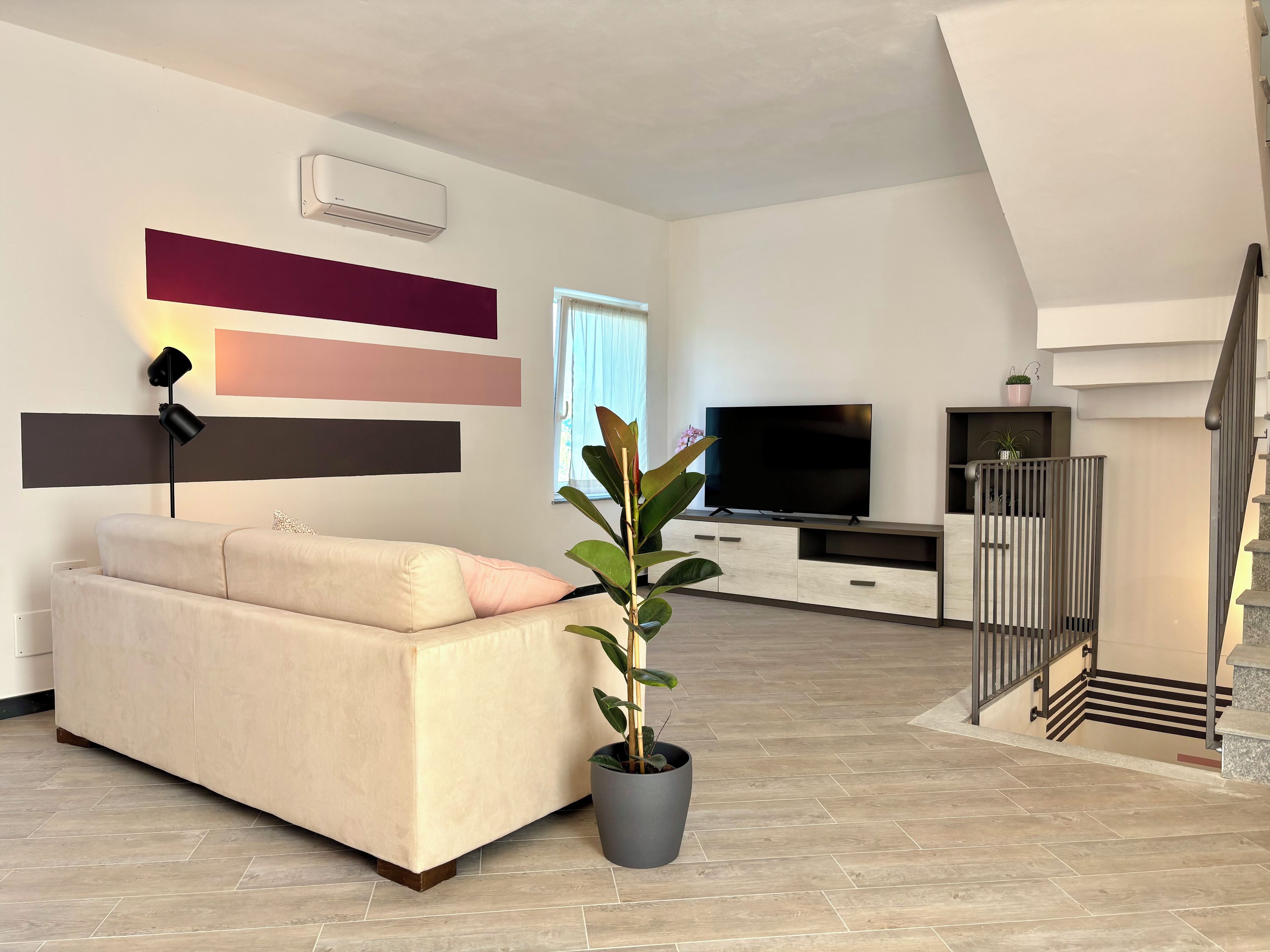 Una sala de estar moderna con un sofá, un televisor de pantalla plana, una planta en maceta y una escalera.