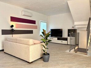 Una sala de estar moderna con un sofá, un televisor de pantalla plana, una planta en maceta y una escalera.