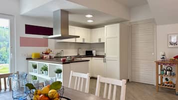 A modern kitchen with white cabinets, a dining table with chairs, and a view of greenery outside.
