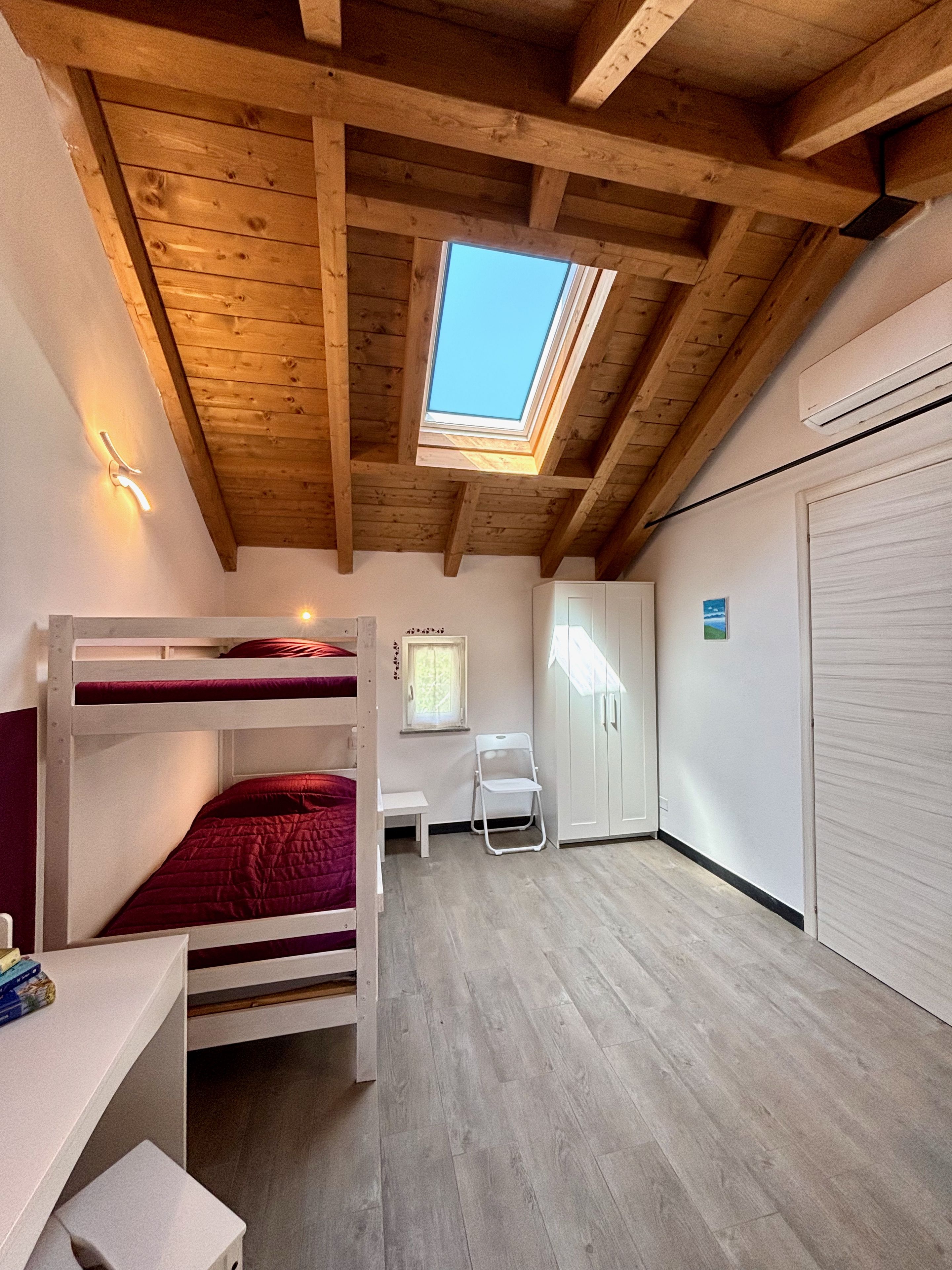 Een kamer met een stapelbed, een bureau, een stoel, een kledingkast en een dakraam.