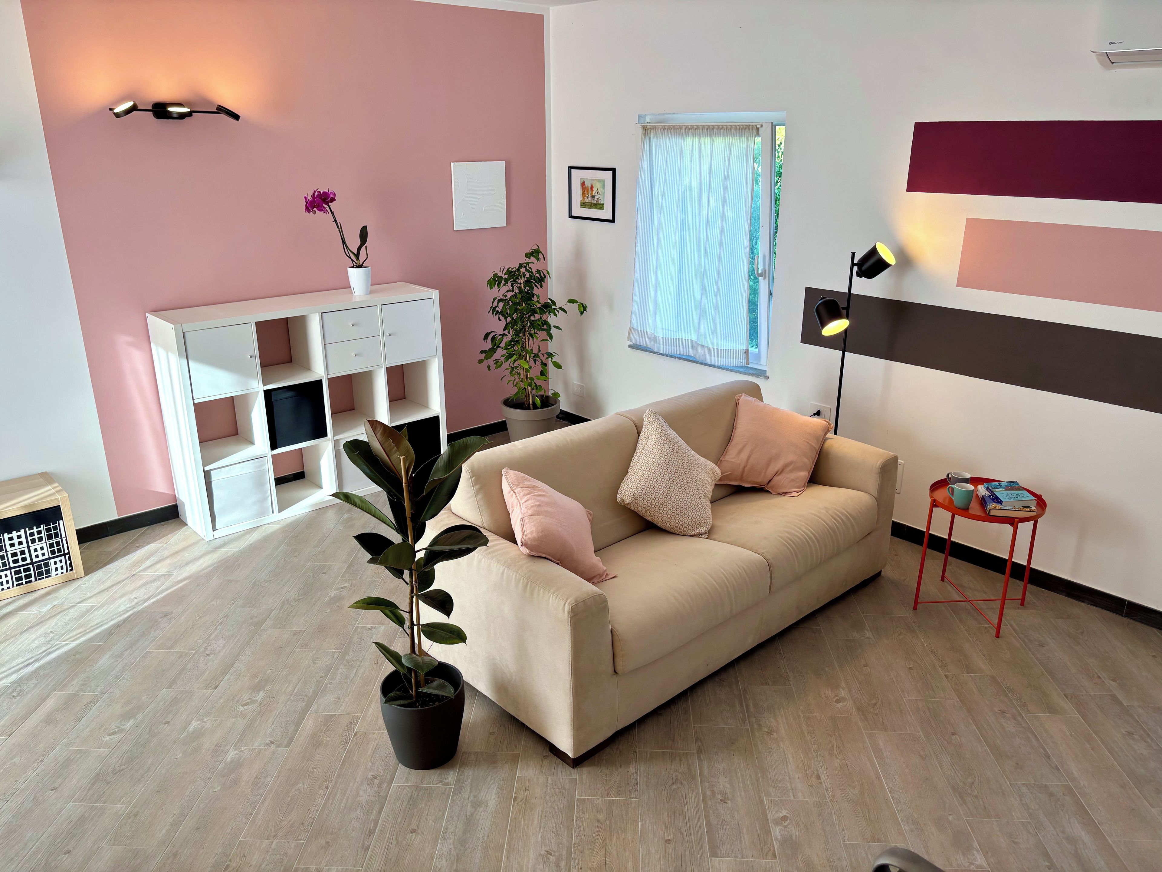 Un salon avec un canapé beige, une plante en pot, un meuble blanc et une petite table rouge sur laquelle sont posés des livres.