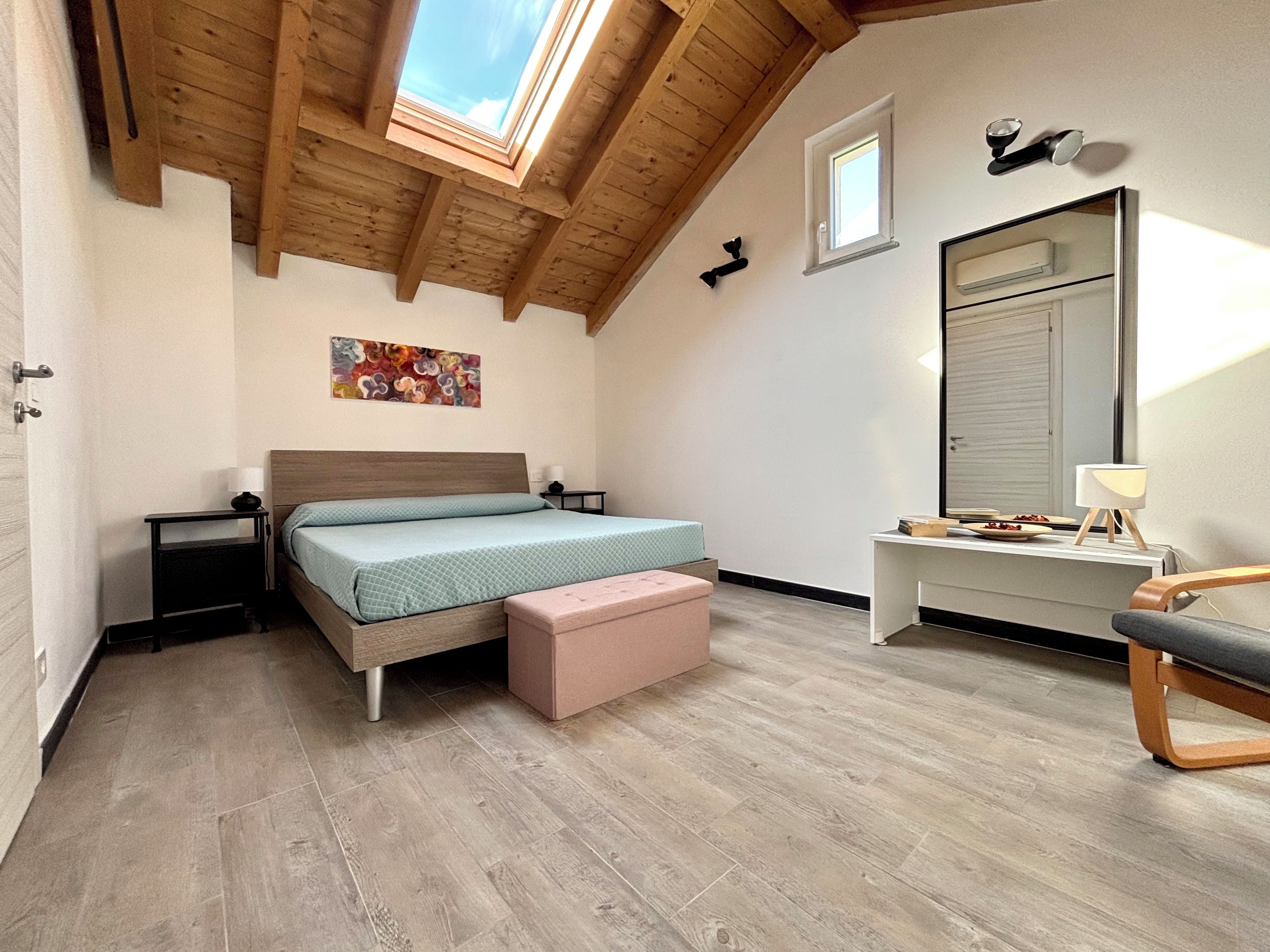 Une chambre avec un plafond en pente, un lit, une table de chevet, un bureau, une chaise et une fenêtre.