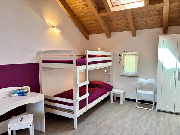 Una cama litera con escritorio y silla, una mesita, un armario y una ventana con persianas.
