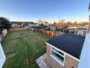 A residential backyard with a grassy lawn, a brick house, and a black roof. - Spacious 3-Bed Home, Sleeps 8, Large Garden, Secure Parking for Multiple Vans (Sutton Bridge)