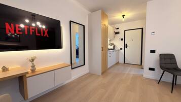 Una sala moderna con un televisor de pantalla plana grande mostrando 'NETFLIX', una consola de madera, un espejo y un sillón gris.