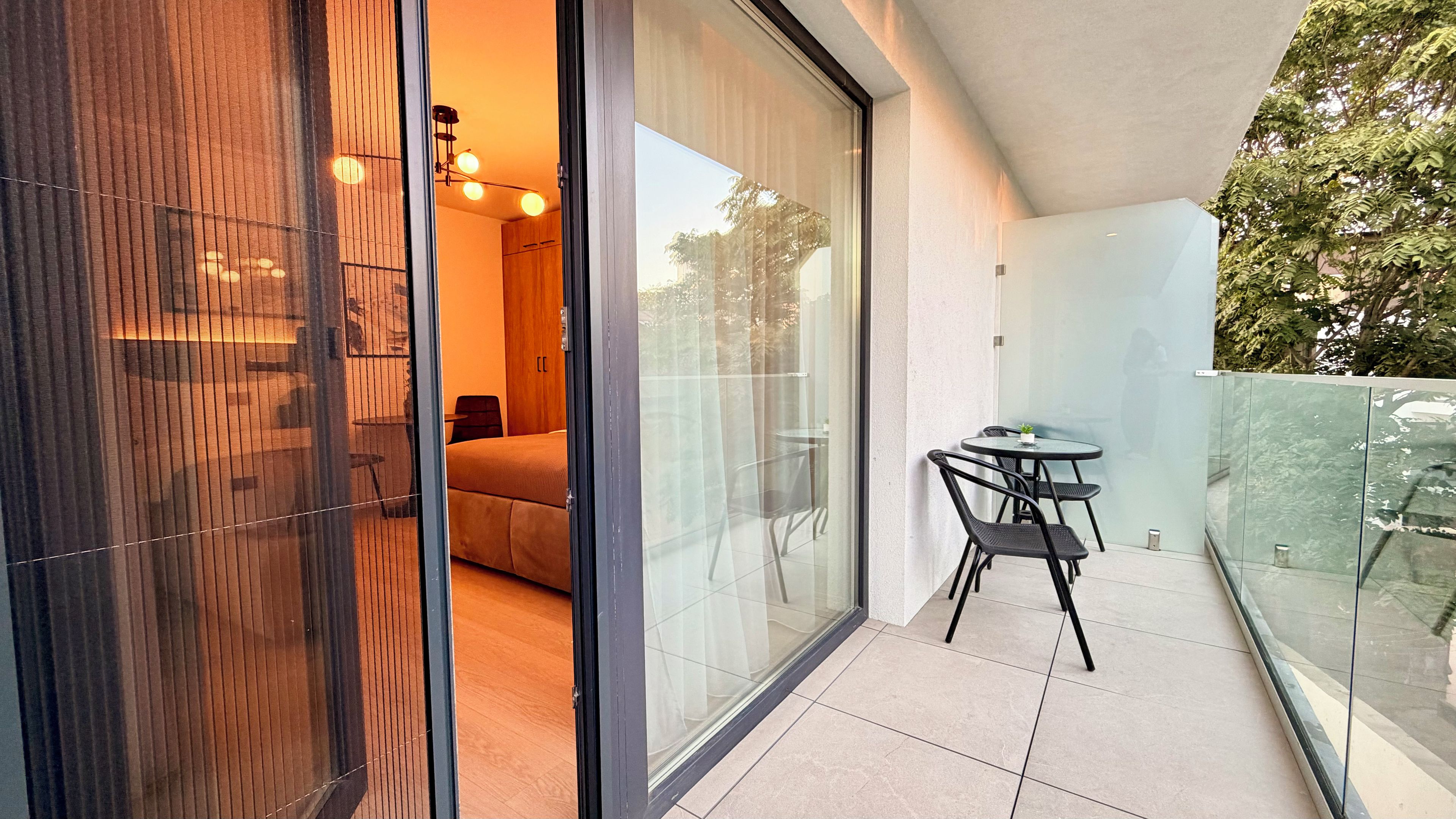 Un balcón moderno con puerta de cristal, una pequeña mesa con sillas y vistas al exterior.