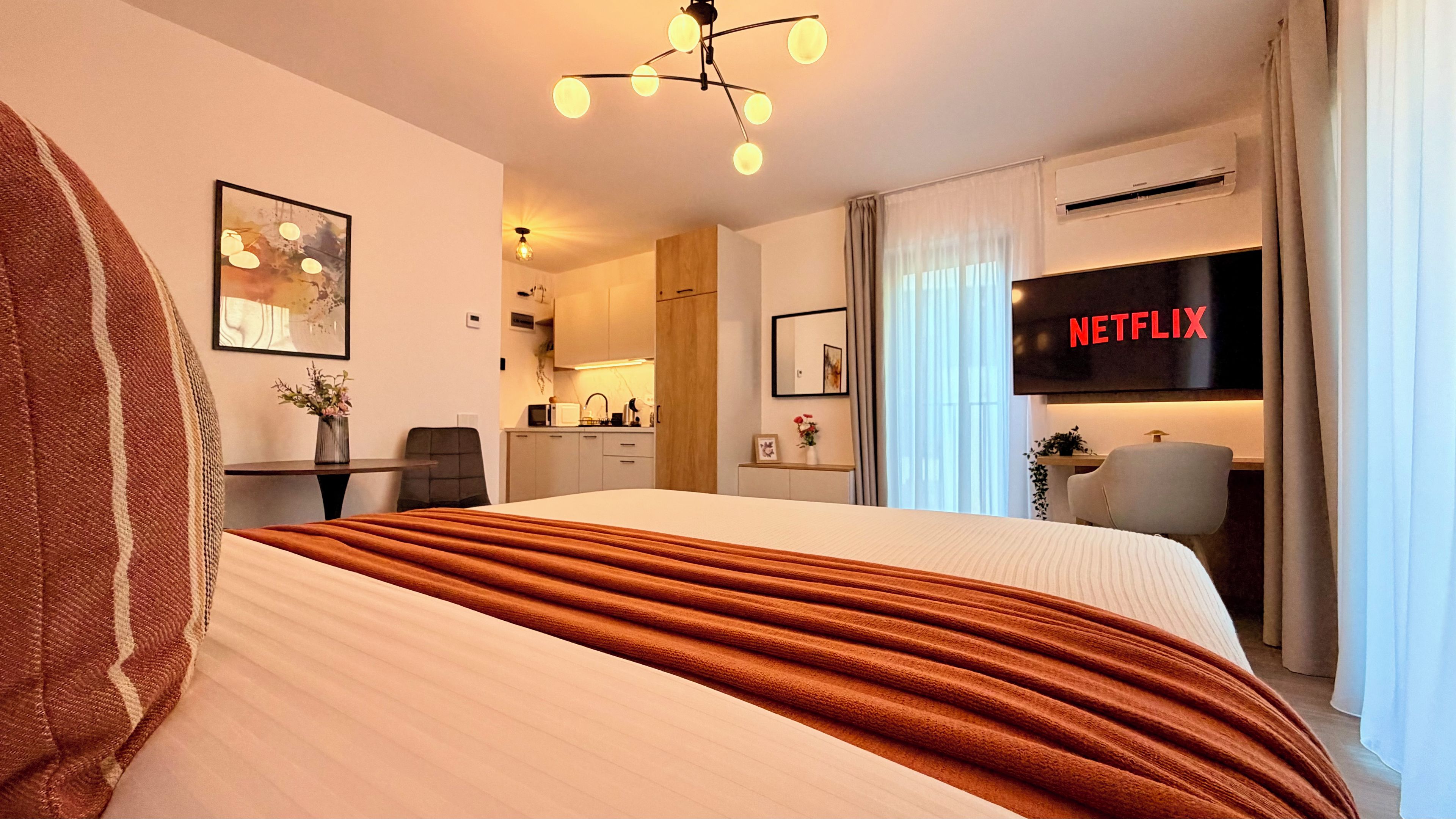 Una habitación de hotel con cama, escritorio, silla, televisor y kitchenette.