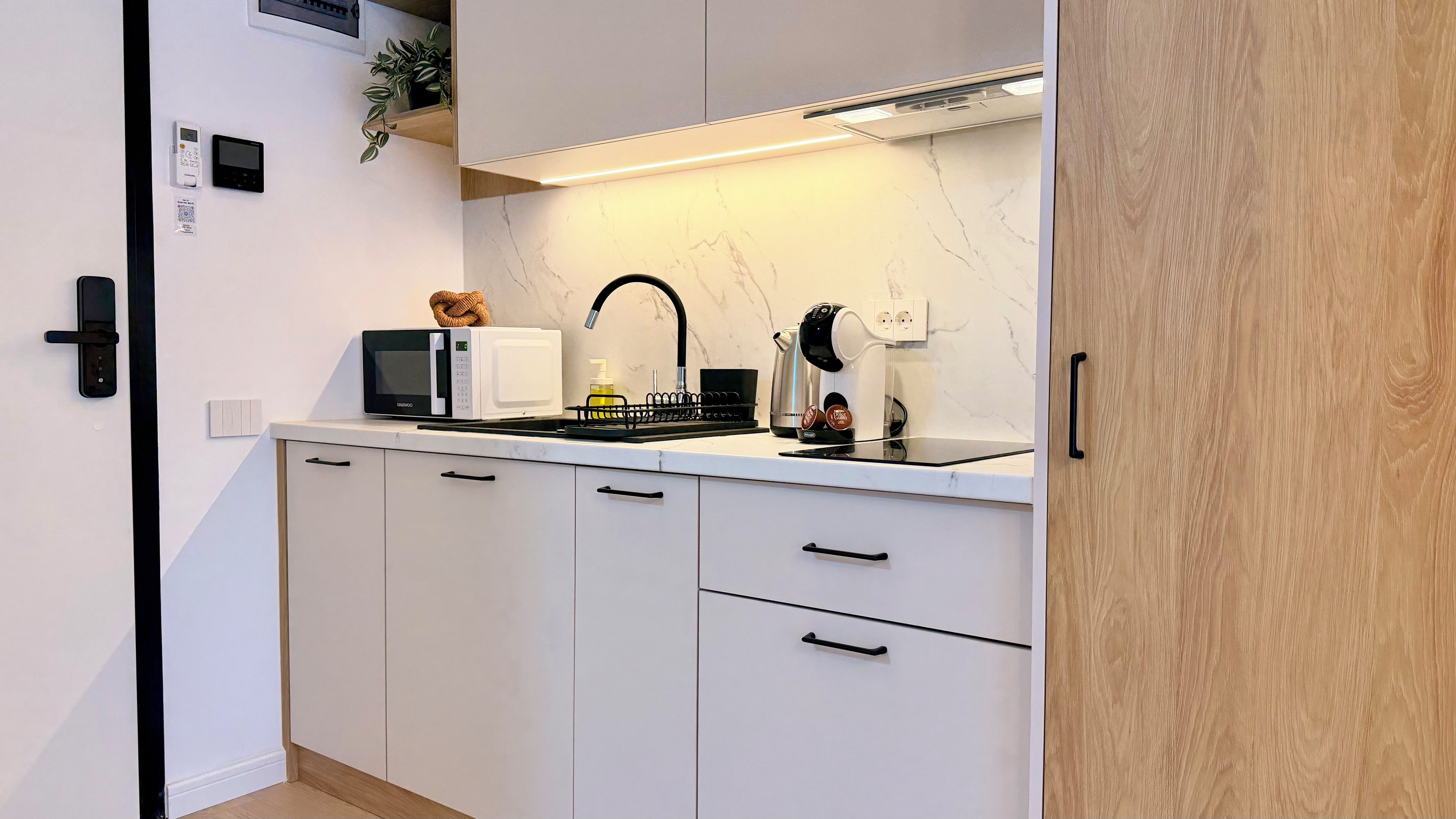 A modern kitchen with white cabinetry, a black faucet, a microwave, and a kettle.