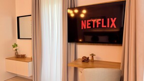 A modern living room with a flat-screen TV displaying 'NETFLIX' on the wall, a wooden console table, a small plant, and a decorative mushroom. - Hubix Suites Icon Studios Exclusive (Bucharest)