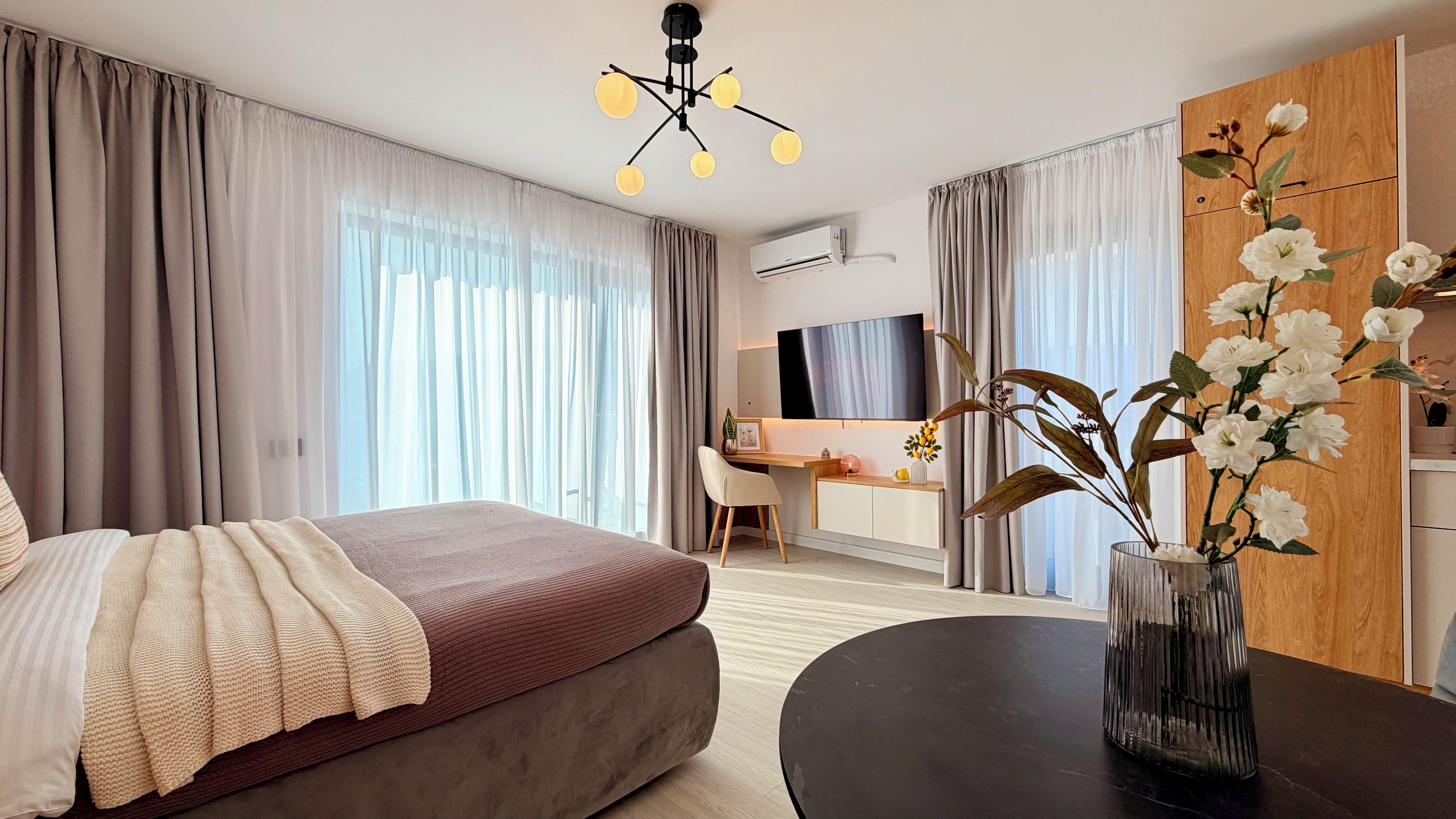 A hotel room with a bed, a desk, a chair, a TV, and a vase with flowers.