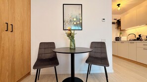 A modern dining area with a round table, two cushioned chairs, a vase with flowers, and a framed artwork on the wall. - Hubix Suites Icon Studios Exclusive (Bucharest)