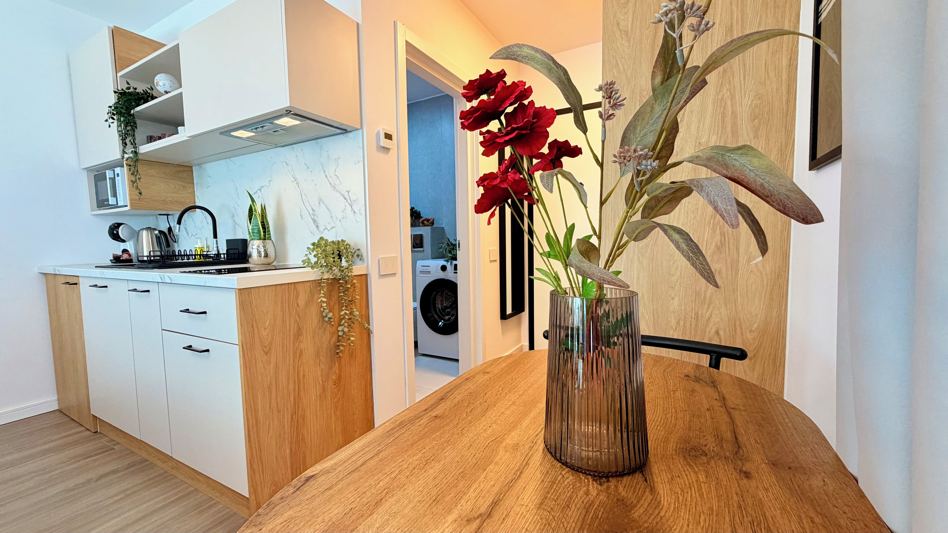 Una cocina moderna con armarios blancos, una encimera de madera y un jarrón con flores rojas.