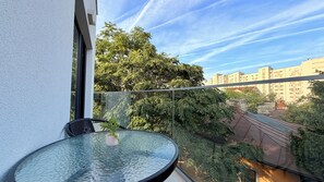 A balcony with a glass table and chair, overlooking a cityscape with buildings and trees. - Hubix Suites Icon Studios Exclusive (Bucharest)