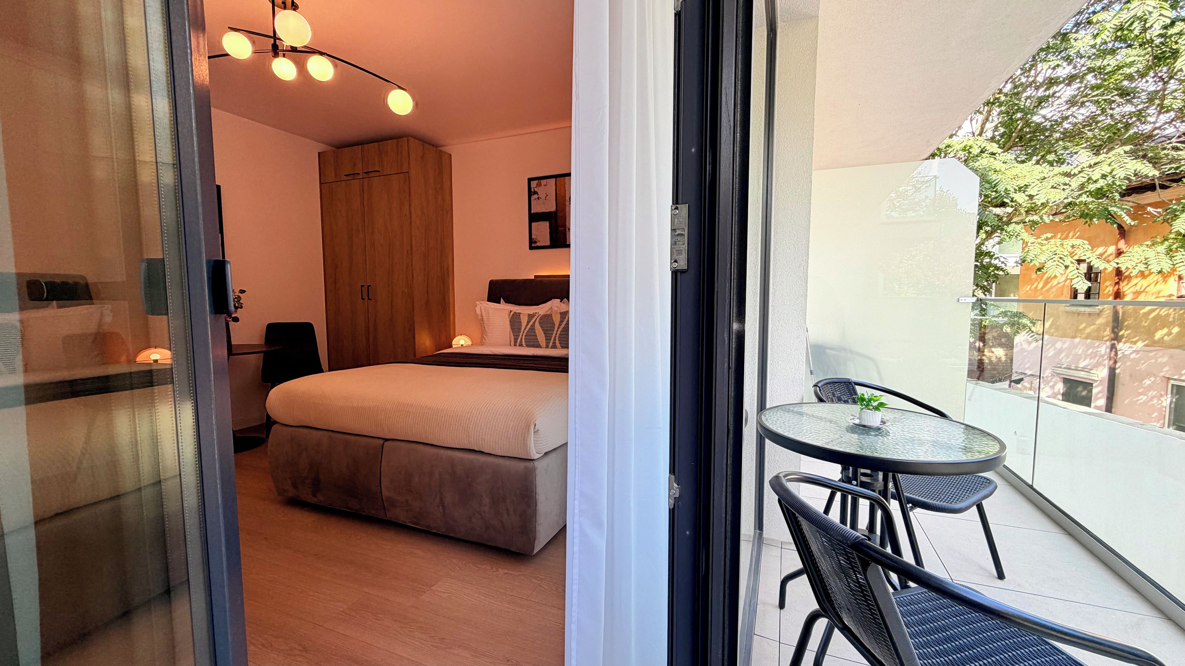 Un dormitorio con cama, armario y mesita de noche. Cuenta con un balcón con mesa y sillas.
