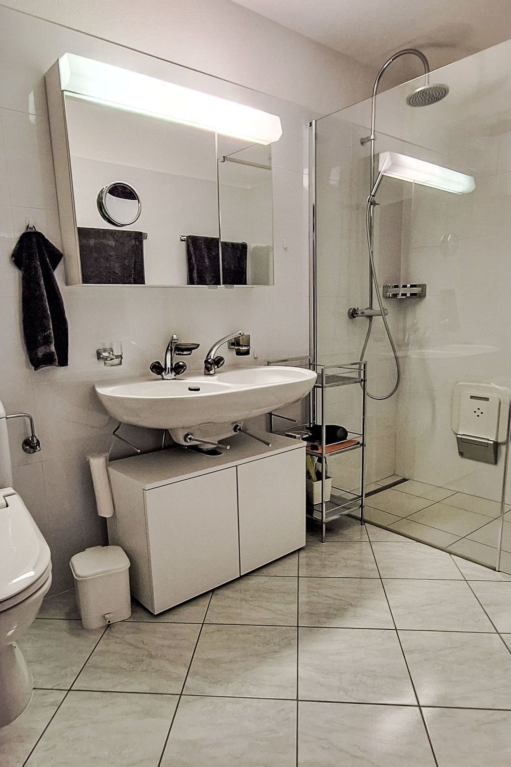 Un baño moderno con un lavamanos blanco, un espejo, cabina de ducha de vidrio y un inodoro.