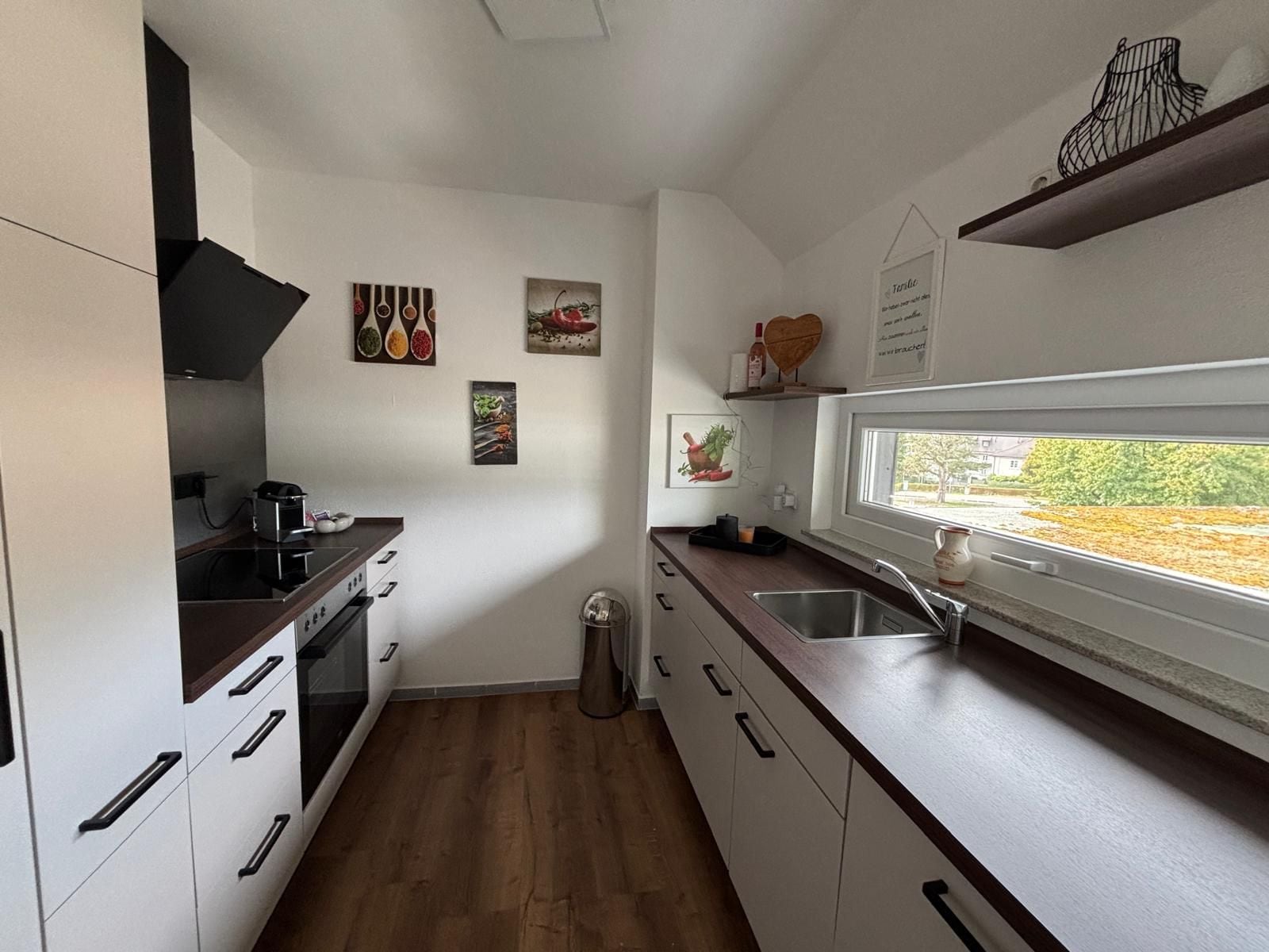 Une cuisine moderne avec des meubles blancs, un plan de travail en bois et une fenêtre offrant une vue agréable.