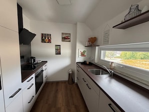 A modern kitchen with white cabinets, a wooden countertop, and a window providing a view.