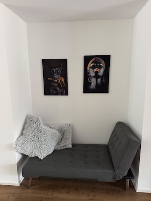 A grey sofa with two fluffy pillows and two framed artworks on the wall.