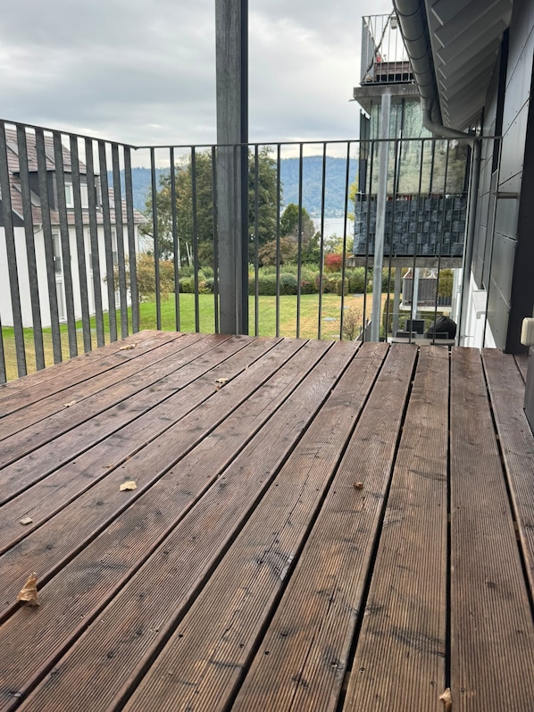 A wooden deck with a metal railing, overlooking a landscaped area with trees and a building in the background.