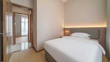 Habitación de hotel con una cama grande, una mesita de noche, una puerta y vista al pasillo.