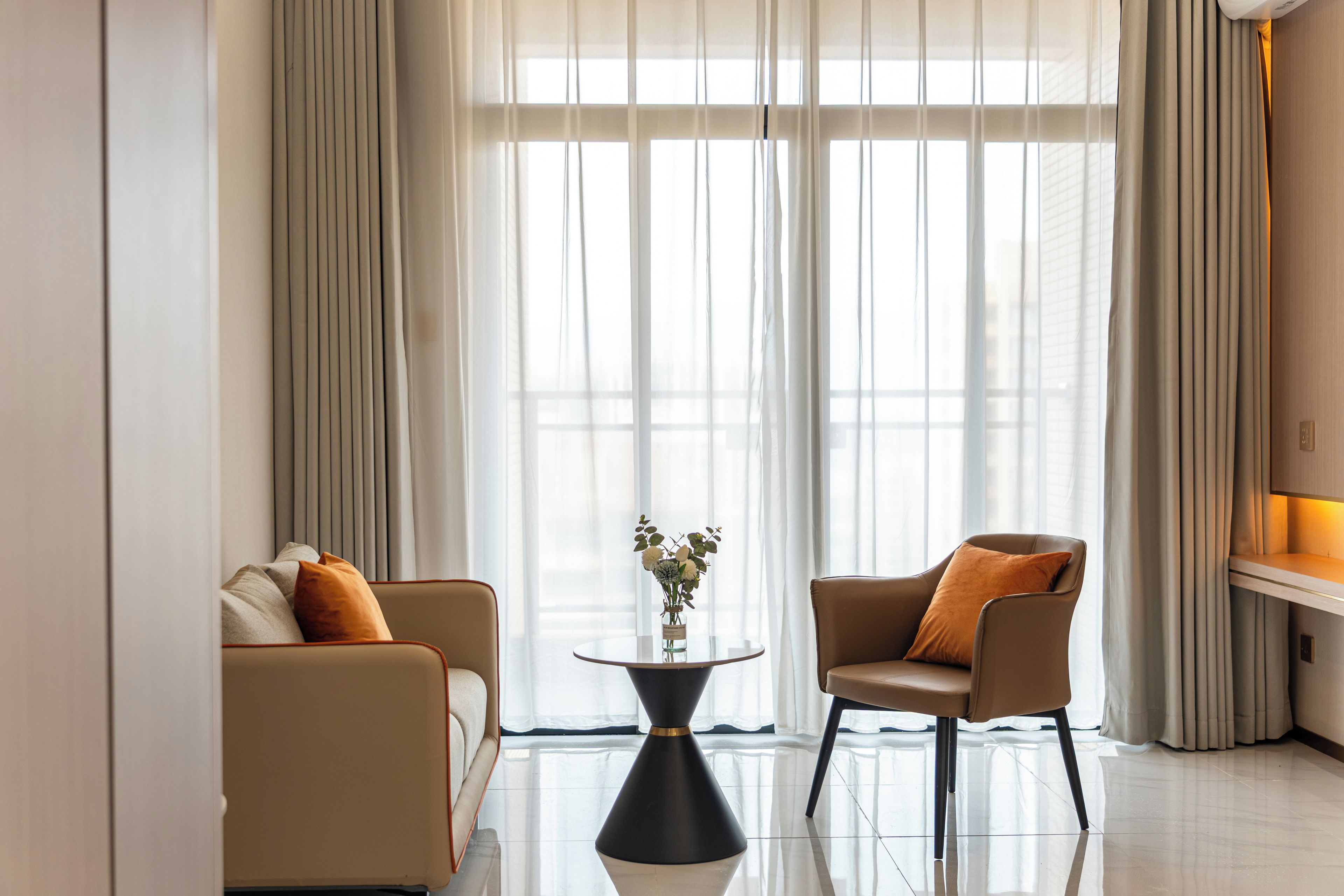 Una sala de estar moderna con un sofá, un sillón y una pequeña mesa redonda con un jarrón de flores.