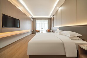 A hotel room with a large bed, a flat-screen TV mounted on the wall, a desk with a chair, and a window with curtains. - Poltton International ApartmentsQingyuan (Qingyuan)