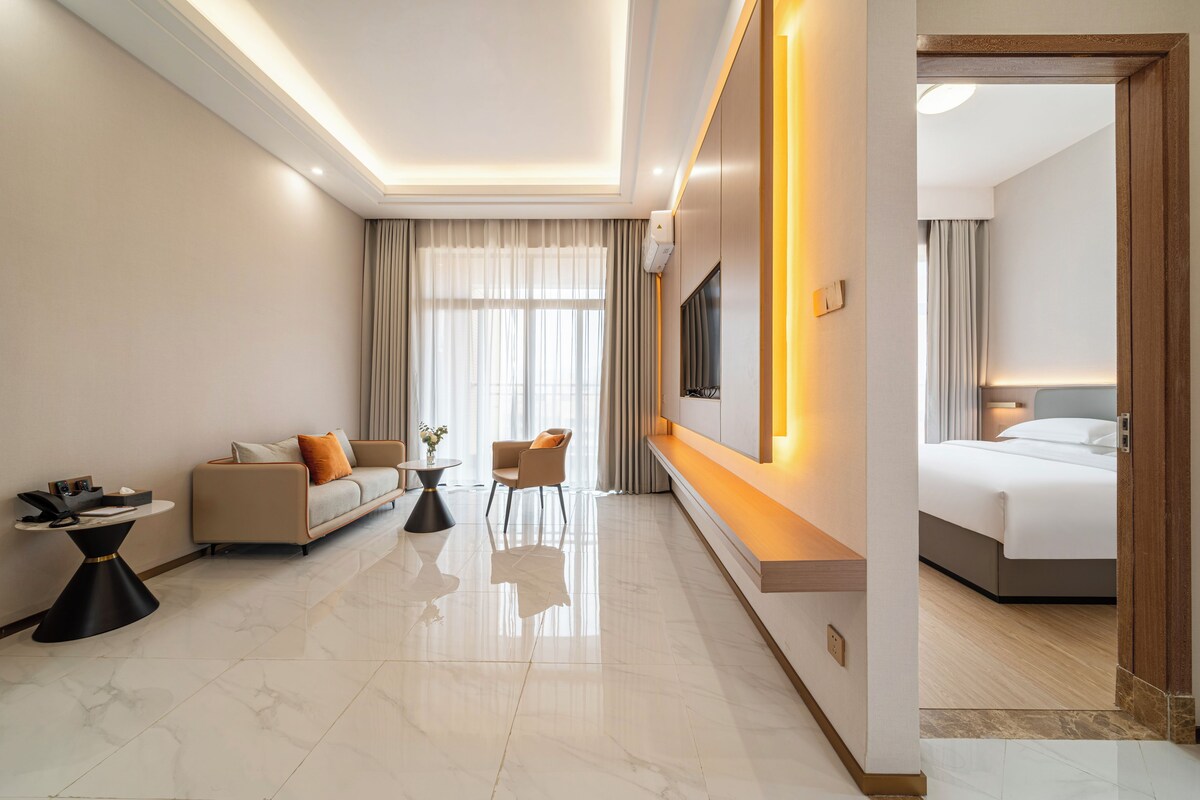A modern hotel room with a sofa, armchair, bedside table, and a bed.
