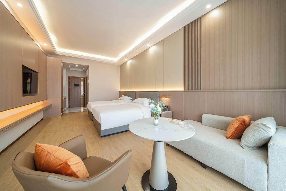 A modern hotel room with a bed, a sofa, a chair, a small table, and a TV.