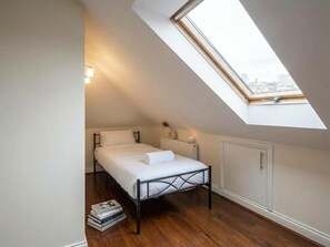 A bedroom with a sloped ceiling, a bed, a radiator, and a window with a view. - St Peters Nest -stylish 1-bed Flat (Croydon)