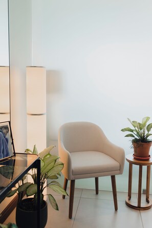 A room with a beige armchair, a round wooden side table with a potted plant, and a floor lamp. - Boutique studio in the heart of SJO with panoramic views & parking (San José)