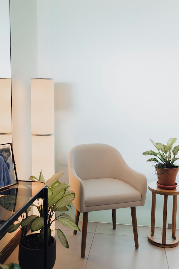 Una habitación con un sillón color beige, una mesita redonda de madera con una planta en maceta y una lámpara de pie.