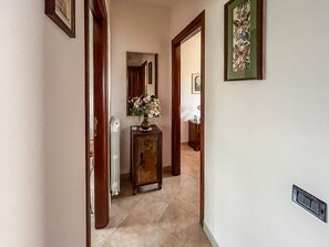 Ein Flur mit einem Heizkörper, einer Holzeinrichtung mit einer Blumenvase und einem gerahmten Kunstwerk an der Wand.