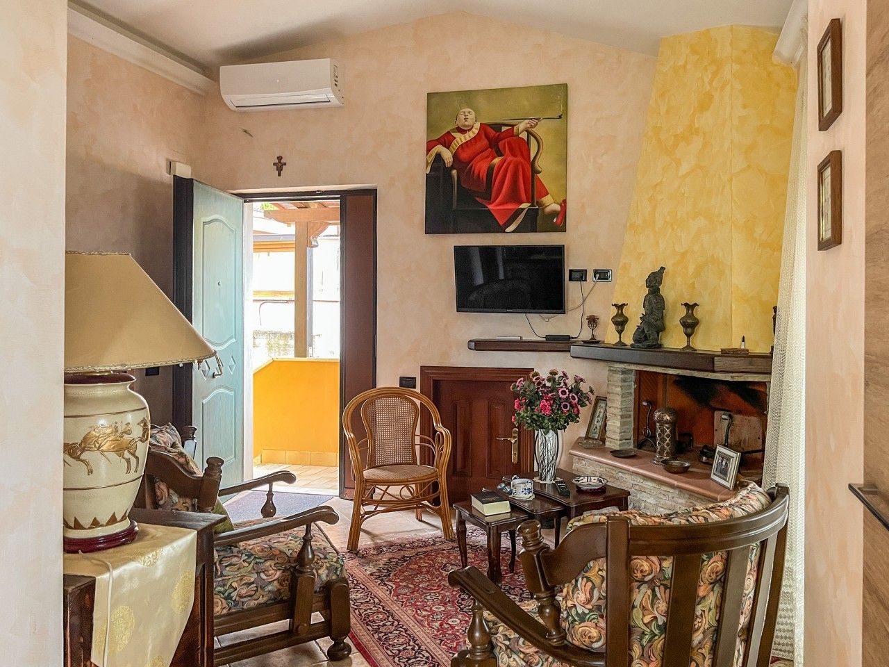 A room with a traditional rattan chair, a wooden table with a vase, and a television mounted on the wall.