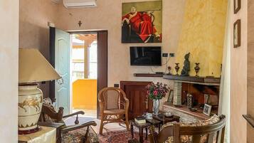 A room with a traditional rattan chair, a wooden table with a vase, and a television mounted on the wall.